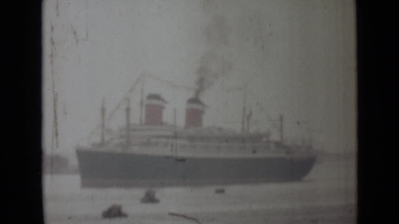 Soft 1946 India 8mm frame of a large steamship seen across water with smoke and small boats nearby.