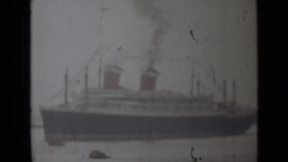 Soft, faded 8mm frame from India in 1946 showing the ship's dark hull, two funnels, light upper decks, and harbor water.