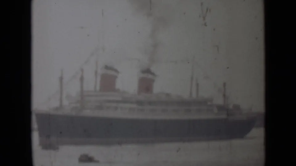 Faded 1946 India home-movie frame showing the two-funneled passenger ship closer in view, with smoke and small boats below.