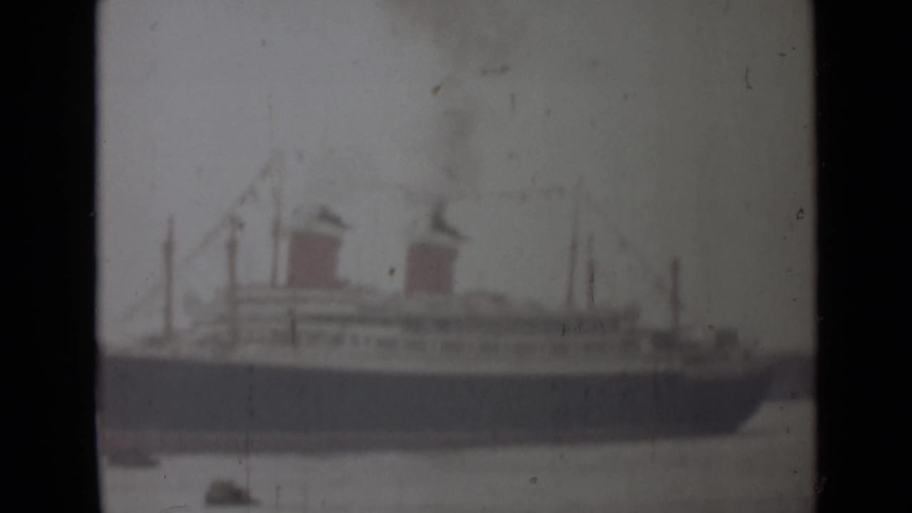 Soft 8mm frame from the 1946 India clip showing the passenger ship in profile, two smoking funnels, and small boats below.