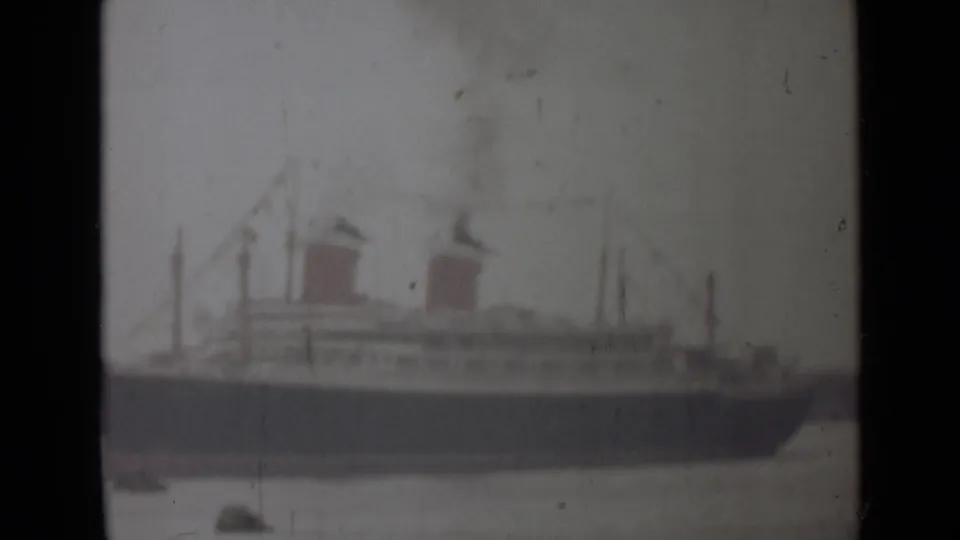 Soft 8mm frame from the 1946 India clip showing the passenger ship in profile, two smoking funnels, and small boats below.