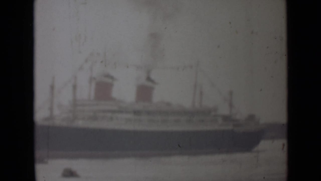 Soft wide view of a large ocean liner with two red funnels beside water.