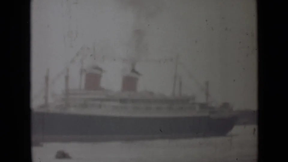 1946 India 8mm frame showing a hazy wide view of a large ocean liner at dock, with red funnels and a dark hull.