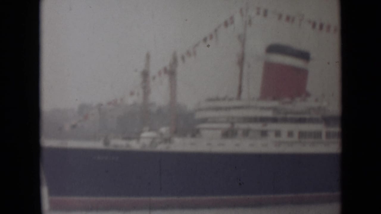 1946 India 8mm frame showing the liner's side, with a red funnel, white deck levels, and decorative flags overhead.