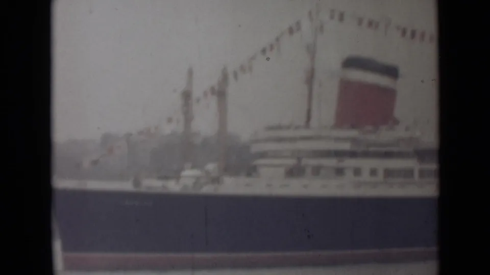 1946 India 8mm frame showing the liner's side, with a red funnel, white deck levels, and decorative flags overhead.