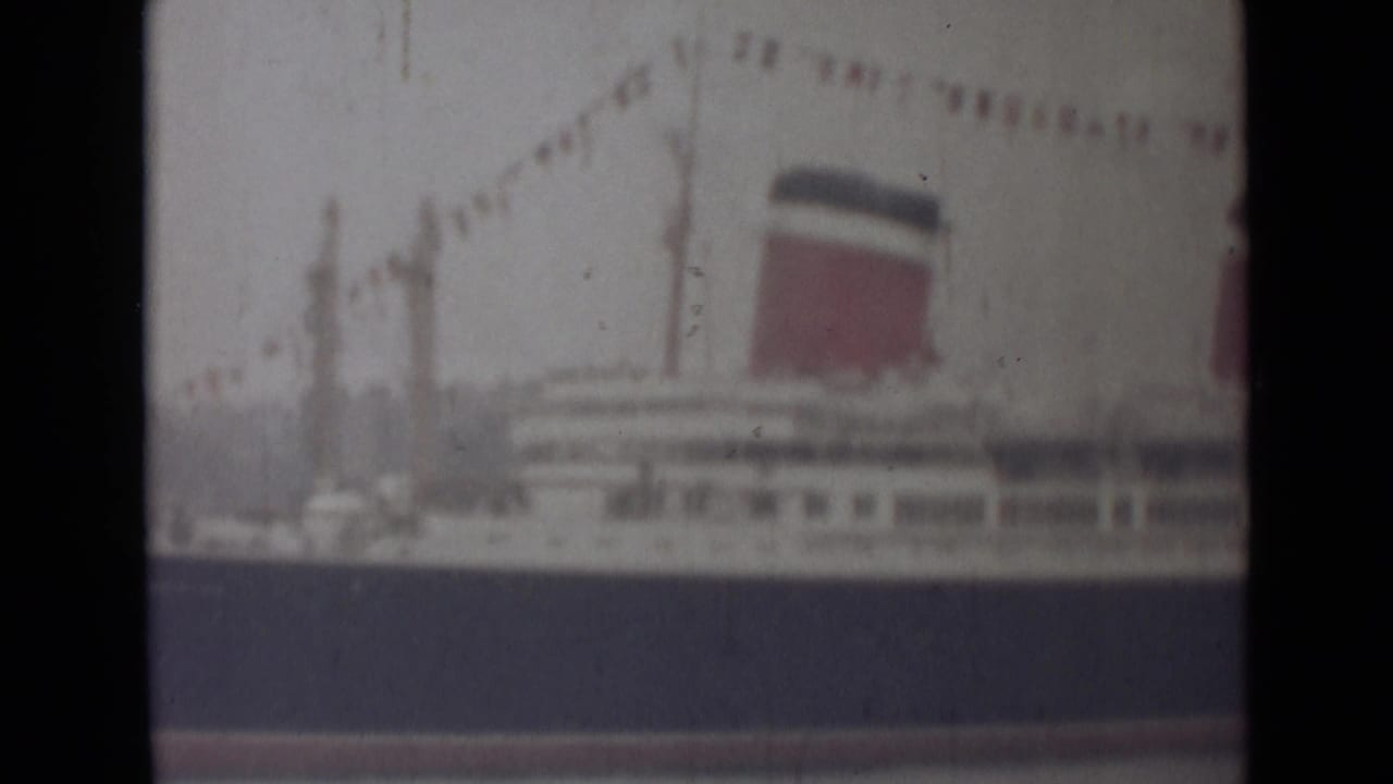 Soft 8mm view of a passenger liner in India, showing deck rows, a red-and-dark funnel and signal flags overhead.