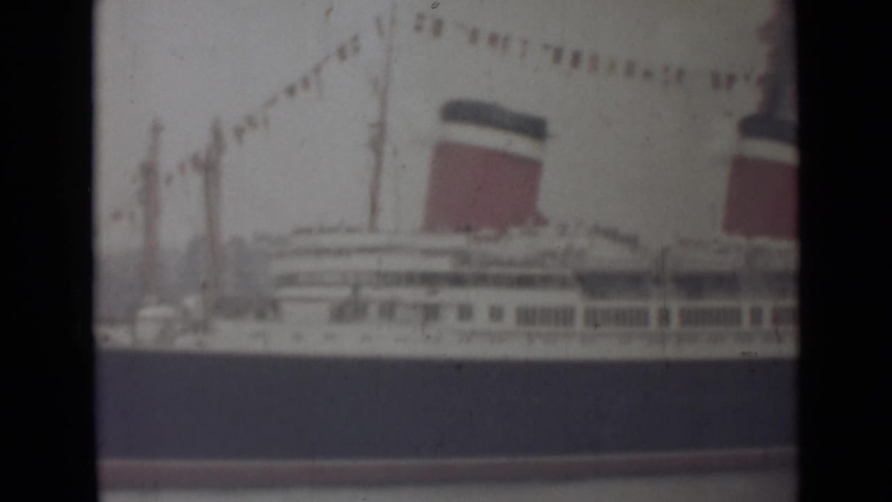 1940s India frame showing the side of a large liner, with one full red-and-dark funnel, a second partial funnel and signal flags.