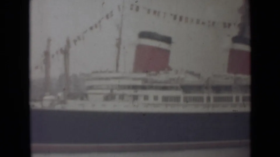 1940s India frame showing the side of a large liner, with one full red-and-dark funnel, a second partial funnel and signal flags.
