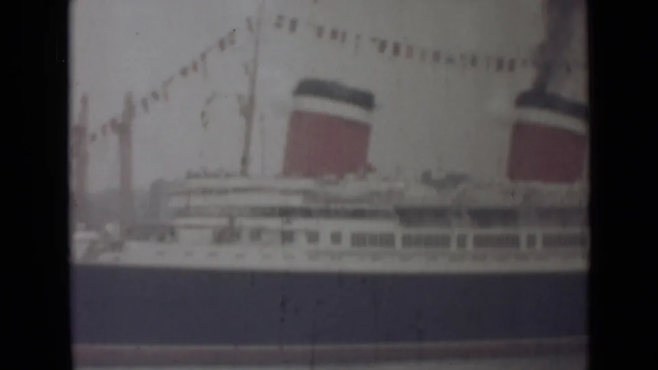 Faded 8mm frame of the India-location liner with flags strung above, deck windows below and two red-and-dark funnels visible.
