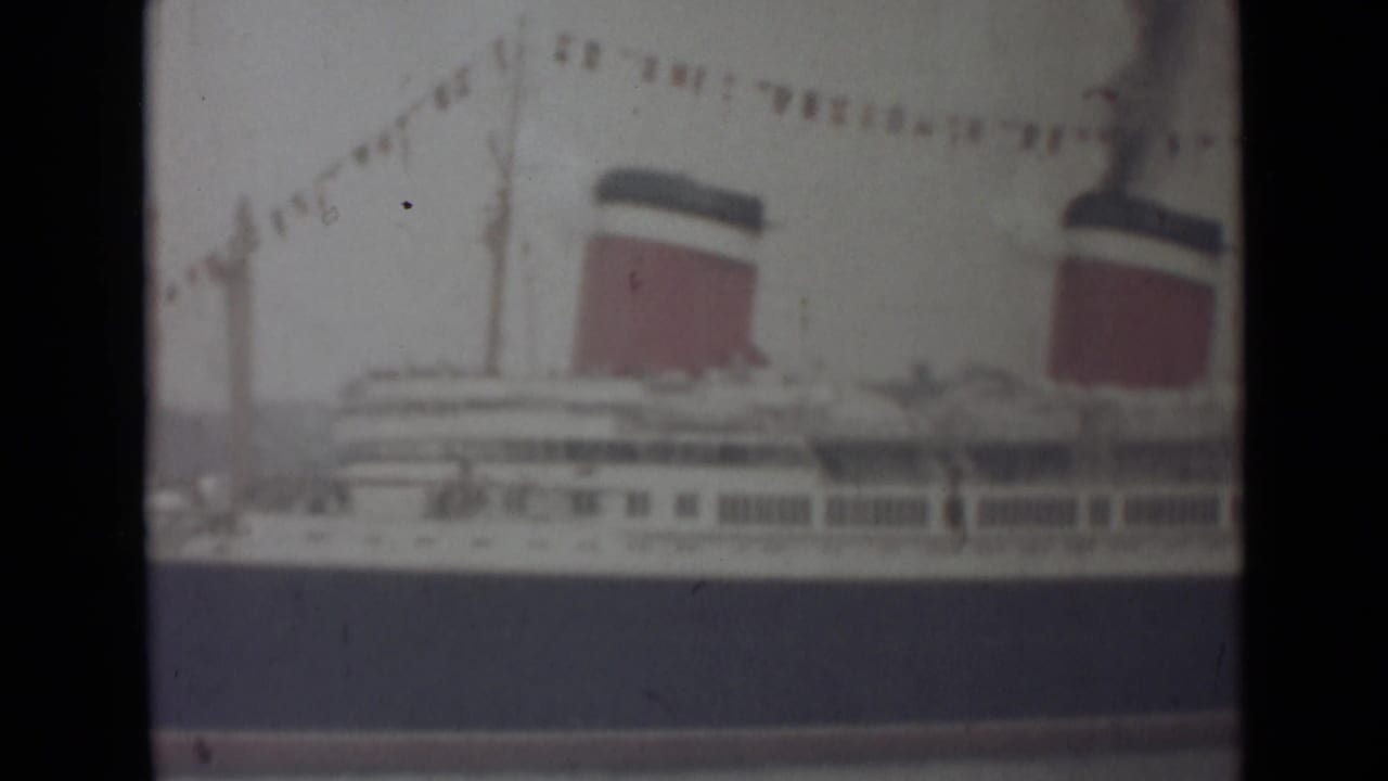 1940s 8mm home-movie view of a docked ocean liner with red-and-black funnels, bunting, and soft faded color.