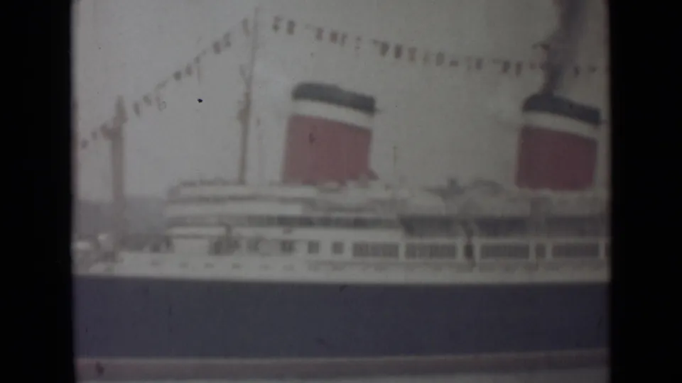 1940s 8mm home-movie view of a docked ocean liner with red-and-black funnels, bunting, and soft faded color.