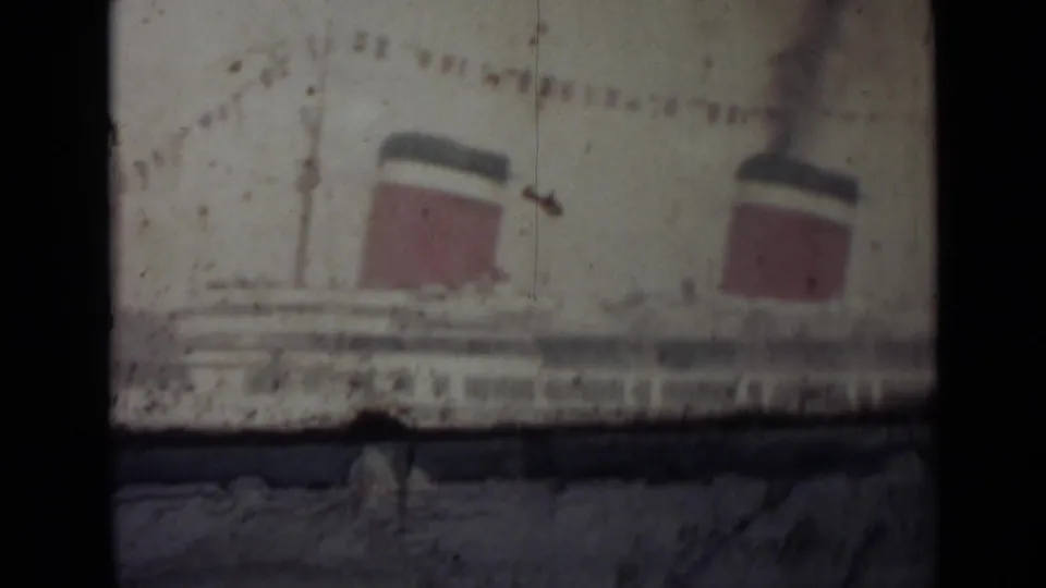 1940s 8mm frame showing the liner's funnels and bunting with heavy gate shadows, scratches, and faded exposure.