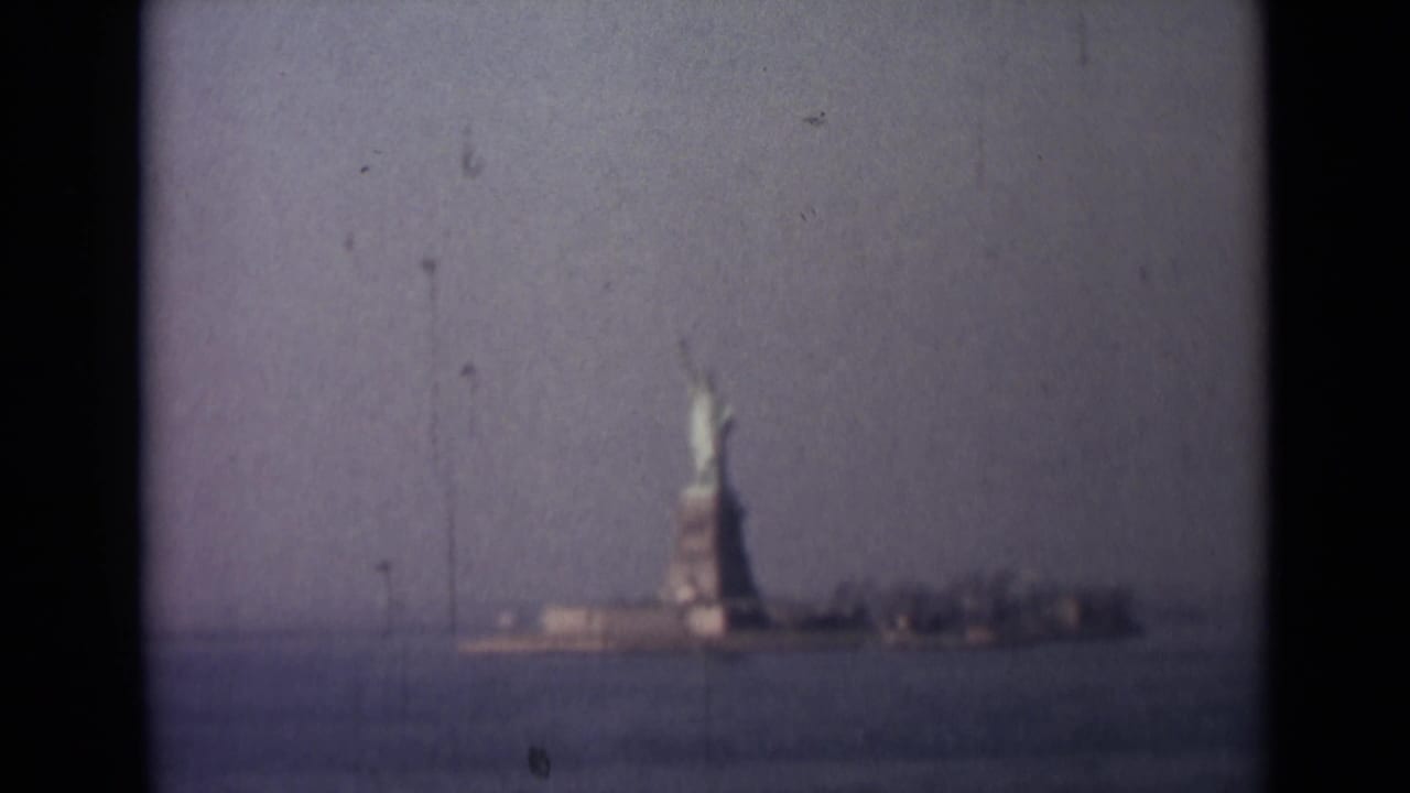 Faded 8mm travel frame of the Statue of Liberty and low shoreline seen from across the harbor.