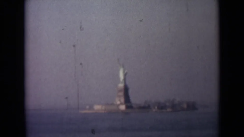 Faded 8mm travel frame of the Statue of Liberty and low shoreline seen from across the harbor.