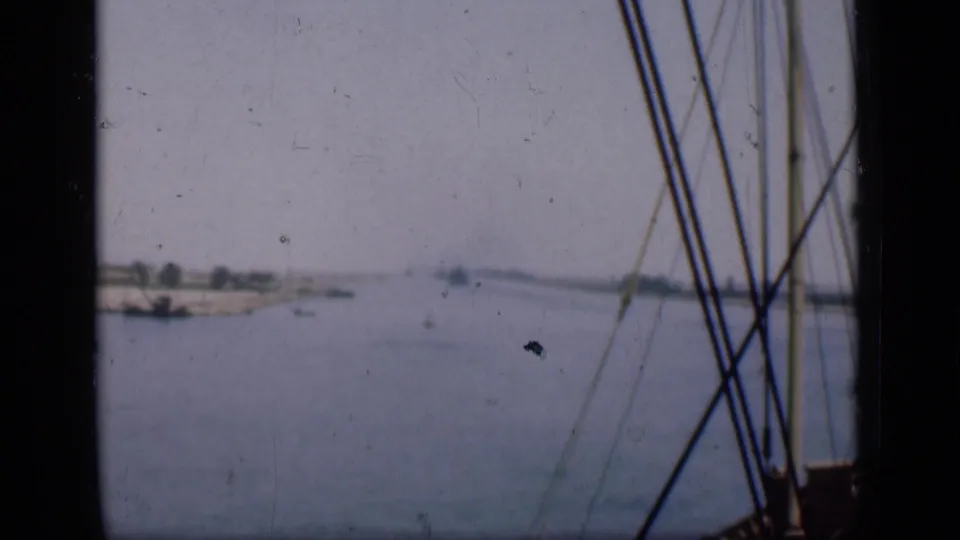 Suez Canal view from a low vessel, with calm water, distant banks and ship rigging in the foreground.