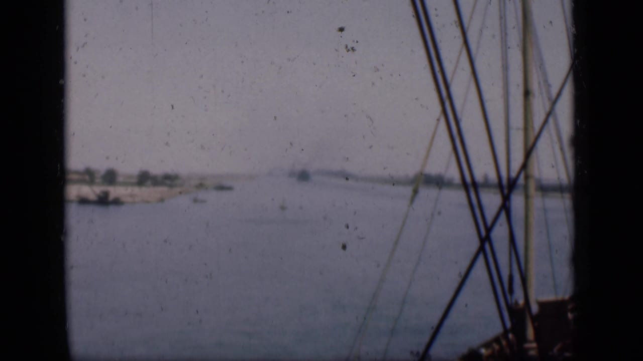 Archival 8mm view of the Suez Canal with a sandy bank, small vessels and foreground rigging from the filming boat.