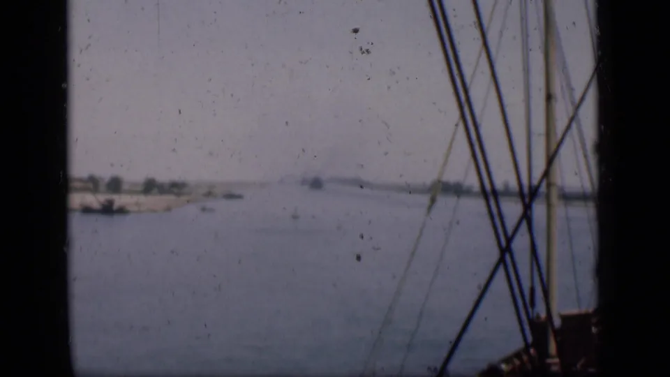 Archival 8mm view of the Suez Canal with a sandy bank, small vessels and foreground rigging from the filming boat.