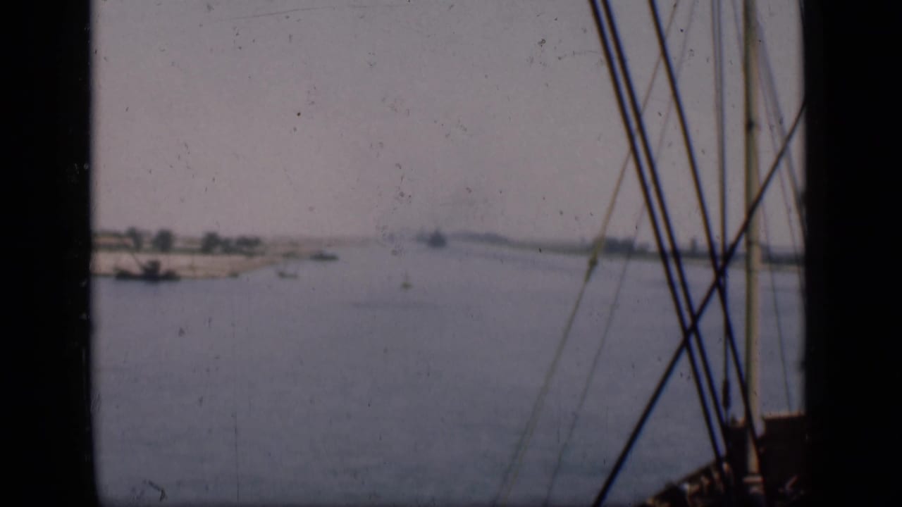 1946 Suez Canal boat view with rigging in the foreground, calm water, low shoreline, and distant vessels.