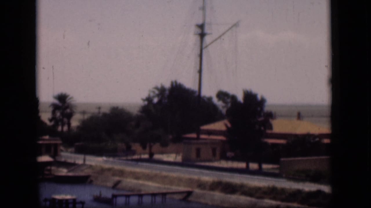 1946 Suez Canal, Egypt frame with a mast above palms and low buildings, seen from a shaded window or opening.