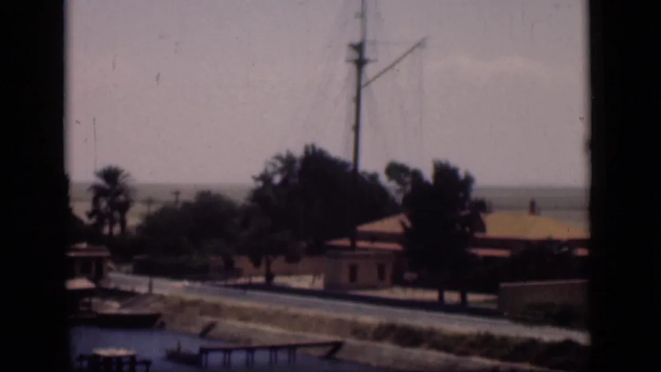 1946 Suez Canal, Egypt frame with a mast above palms and low buildings, seen from a shaded window or opening.