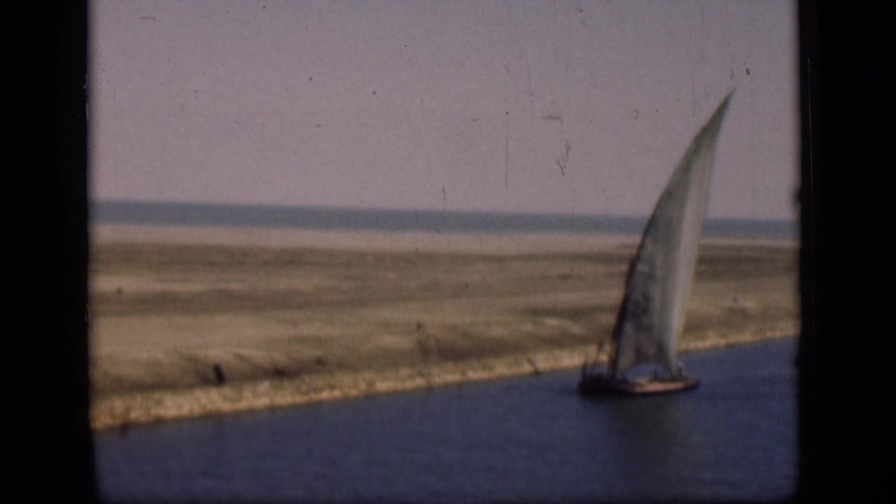 A sailboat with a tall white sail moves along the Suez Canal area in 1946, with grassy banks and open land beyond.