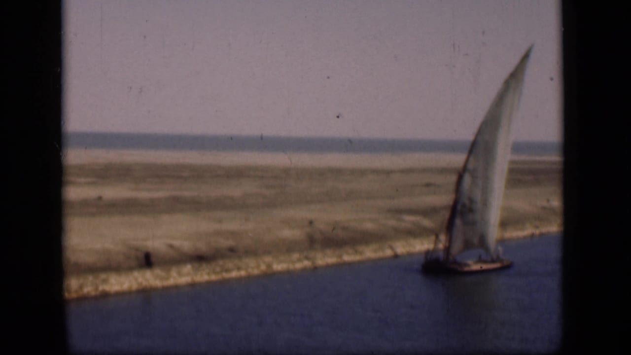 1946 8mm frame of a white-sailed boat on the Suez Canal area, bordered by low banks and open terrain.