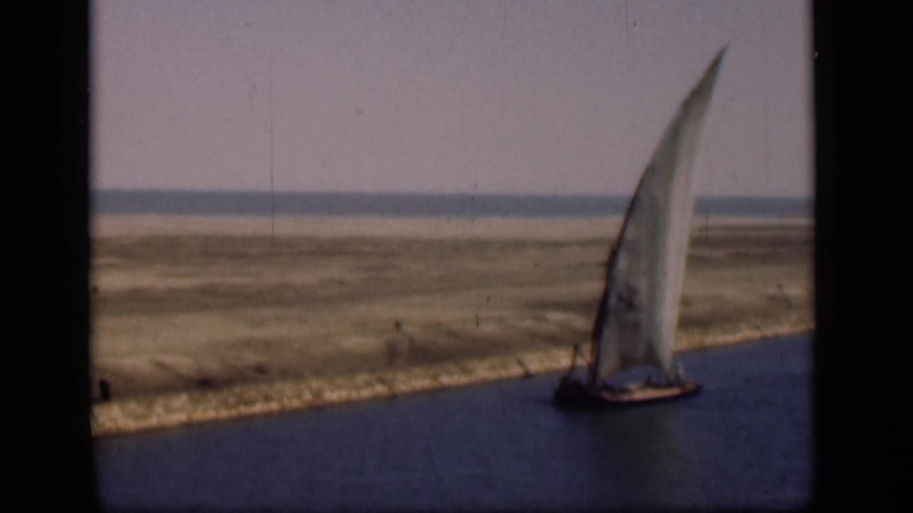 1946 Suez Canal frame with a traditional sailboat near the right edge, calm water in front, and open sandy terrain beyond.