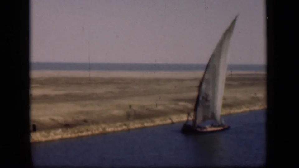 1946 Suez Canal frame with a traditional sailboat near the right edge, calm water in front, and open sandy terrain beyond.