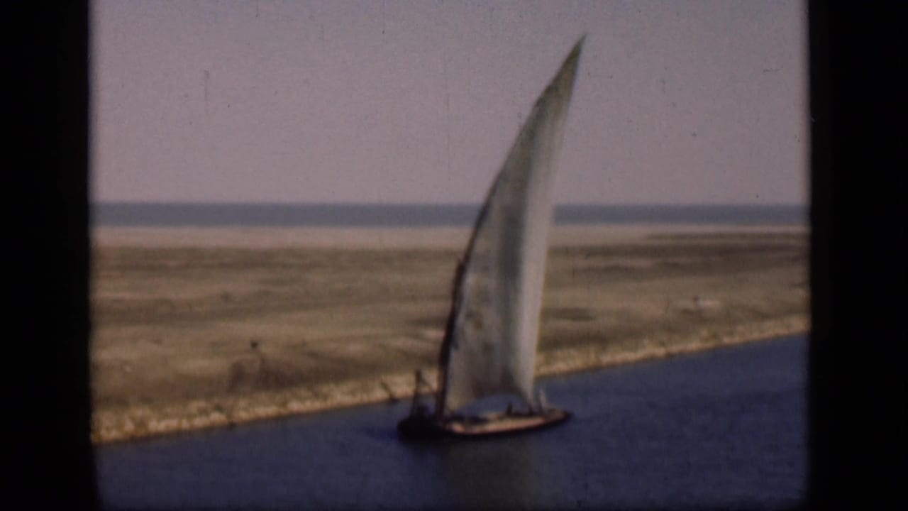 1946 Suez Canal frame showing the sailboat still moving along calm water, with a barren bank and low horizon in the background.