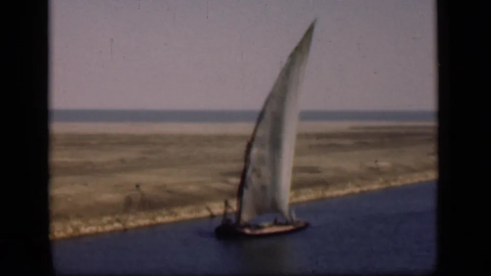 1946 Suez Canal frame showing the sailboat still moving along calm water, with a barren bank and low horizon in the background.