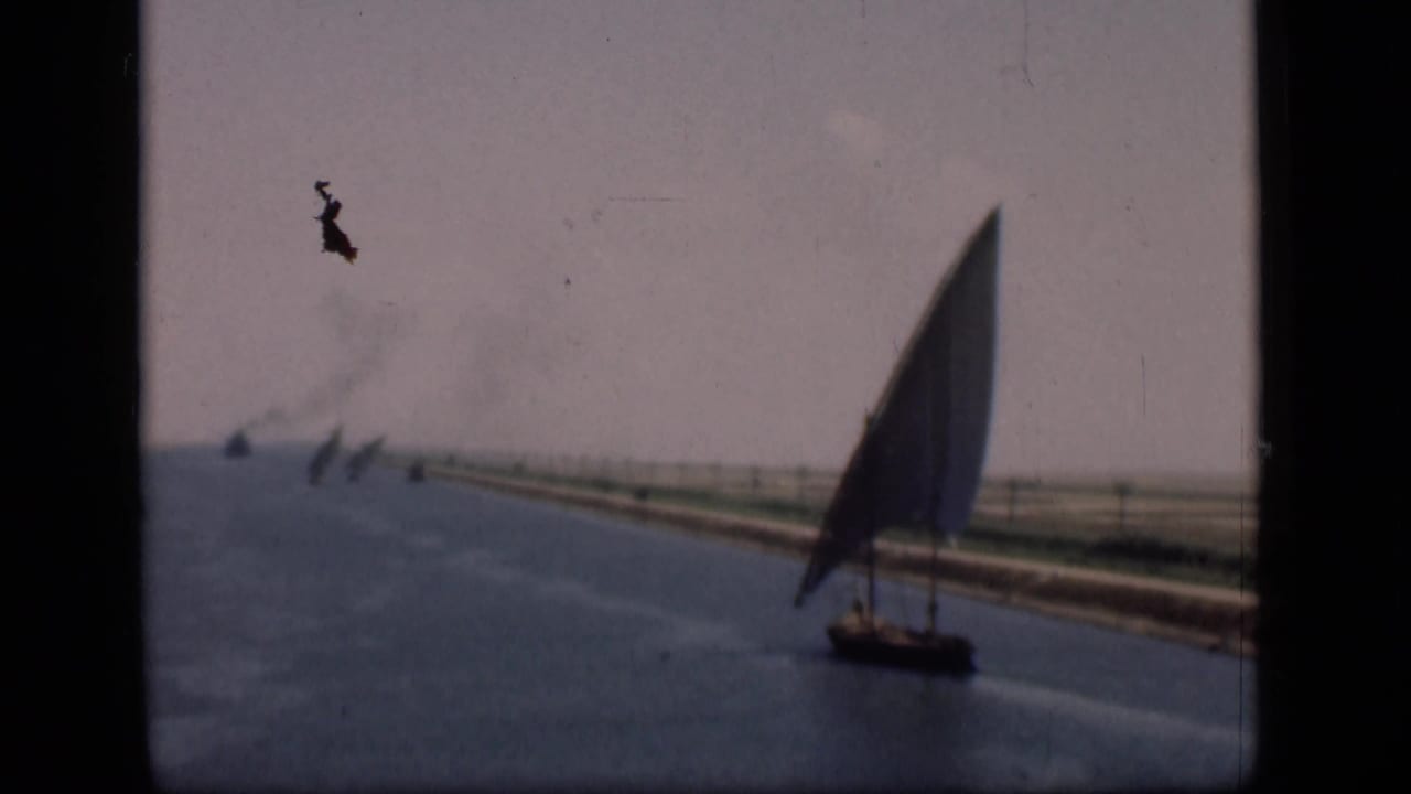 1946 Suez Canal frame showing a tall lateen sailboat near the right side, with low banks, distant sails, smoke, and faded color.