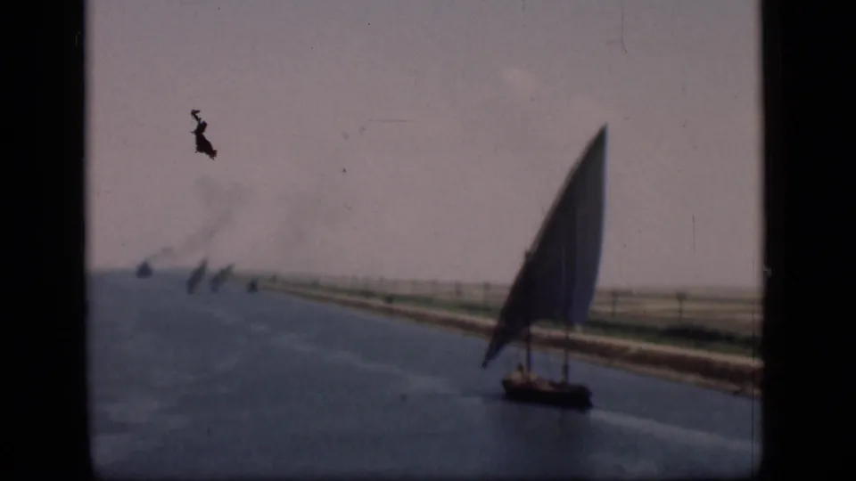 1946 Suez Canal frame showing a tall lateen sailboat near the right side, with low banks, distant sails, smoke, and faded color.