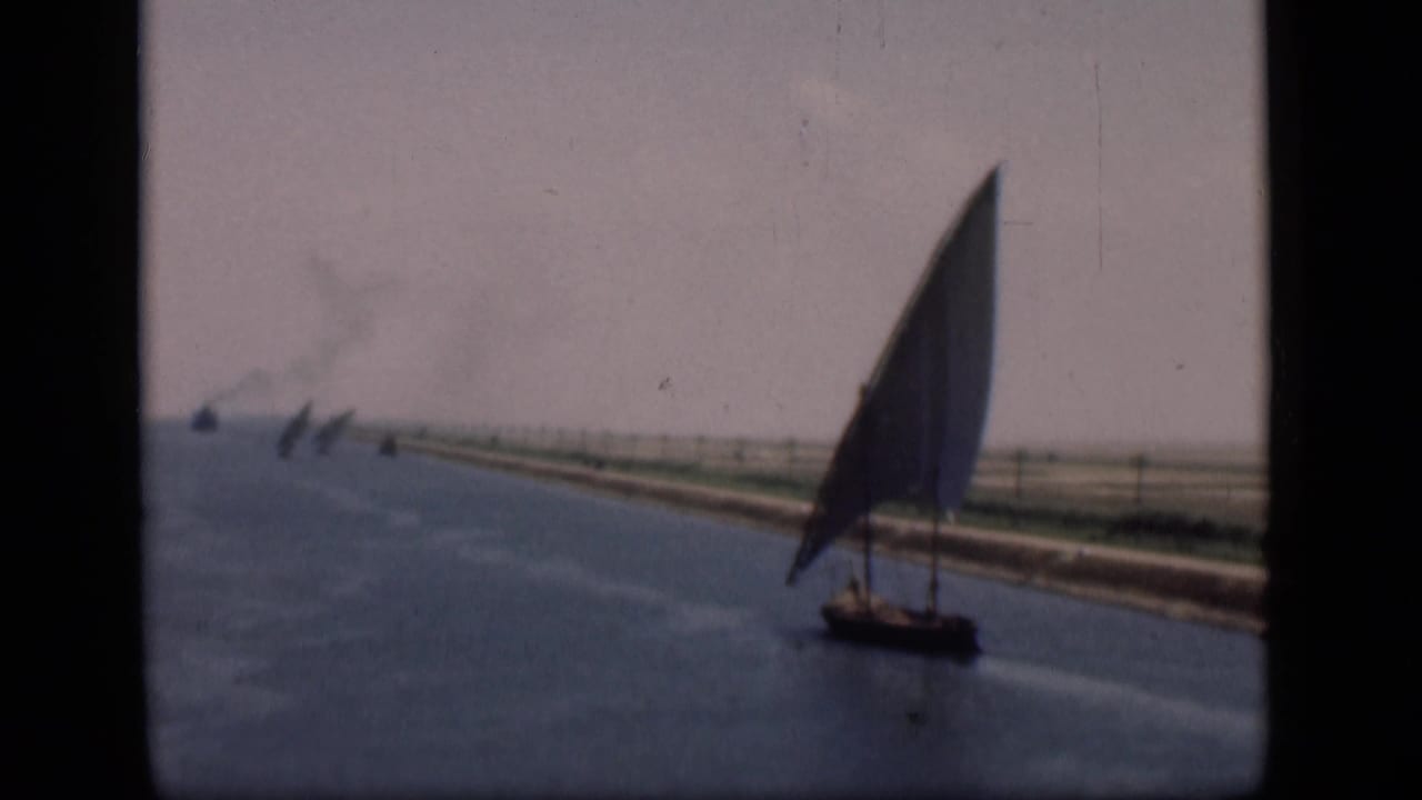 Felucca sailboat on a wide canal with low banks and distant boats.