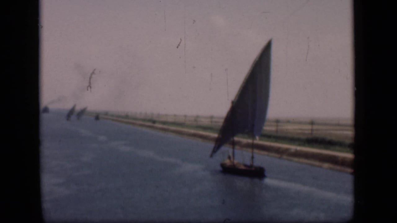 Felucca sailboat on the Suez Canal, filmed in soft 8mm color with flat banks and distant canal traffic.