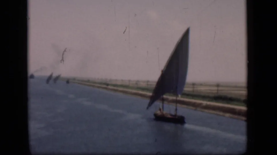 Felucca sailboat on the Suez Canal, filmed in soft 8mm color with flat banks and distant canal traffic.