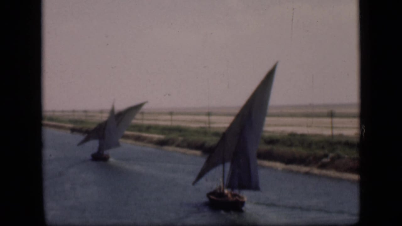 Two felucca sailboats appear on the Suez Canal, one close to camera and another crossing farther back.