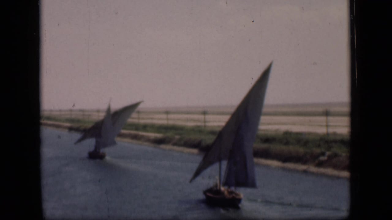 1946 Suez Canal home-movie frame showing two traditional sailboats on calm water with sparse vegetation along the bank.