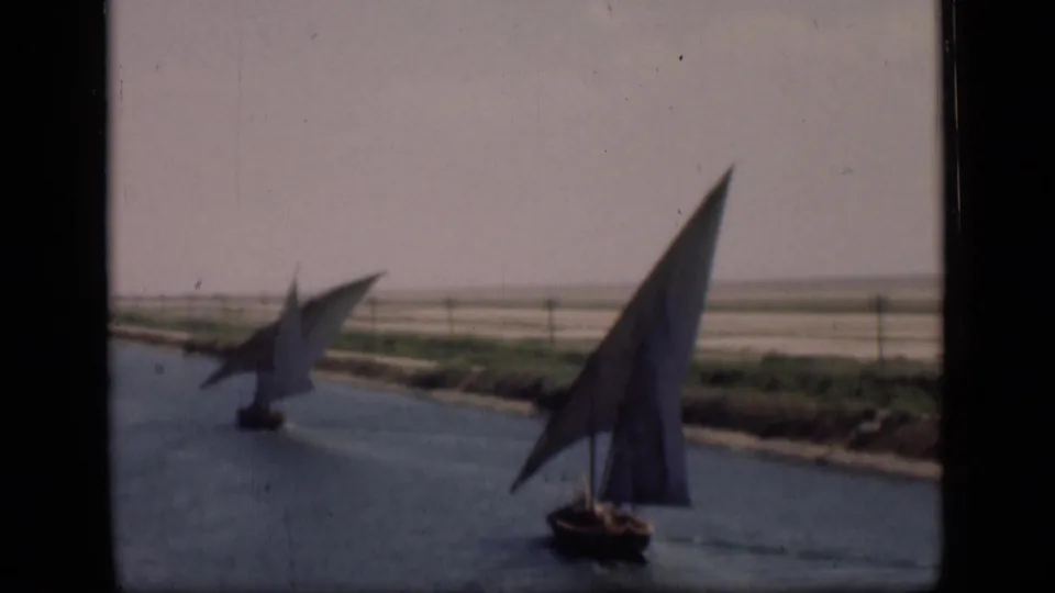 1946 Suez Canal home-movie frame showing two traditional sailboats on calm water with sparse vegetation along the bank.
