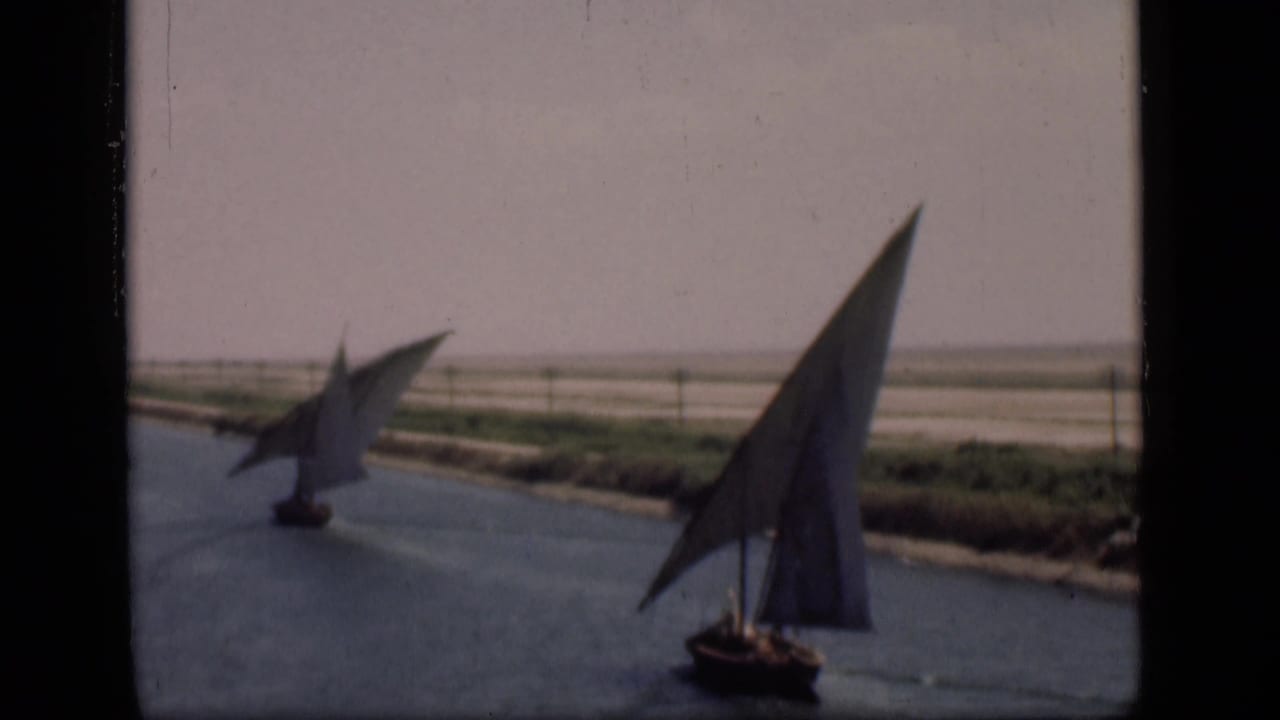 Suez Canal, Egypt, 1946: a near sailboat with a tall triangular sail passes in front of a smaller distant boat.