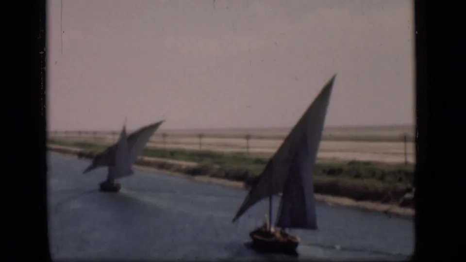 Suez Canal, Egypt, 1946: a near sailboat with a tall triangular sail passes in front of a smaller distant boat.