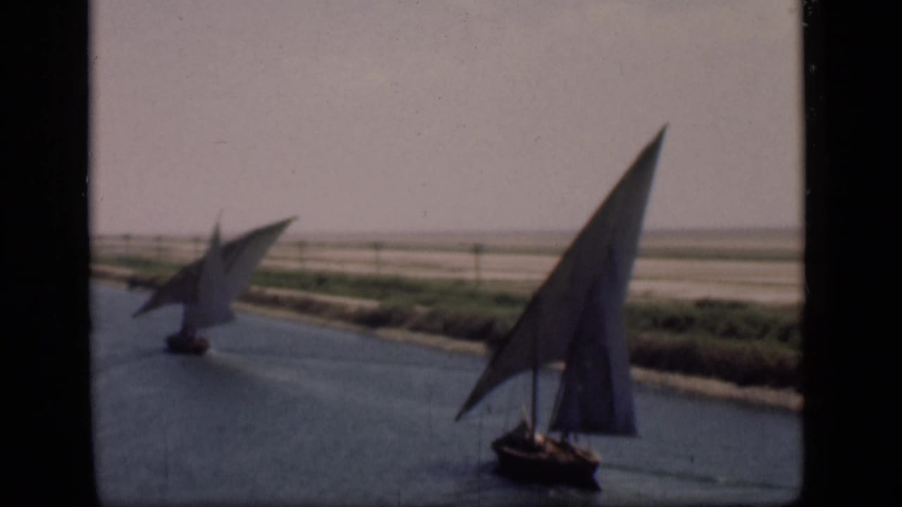 Pair of sailboats on blue canal water with arid flats beyond.