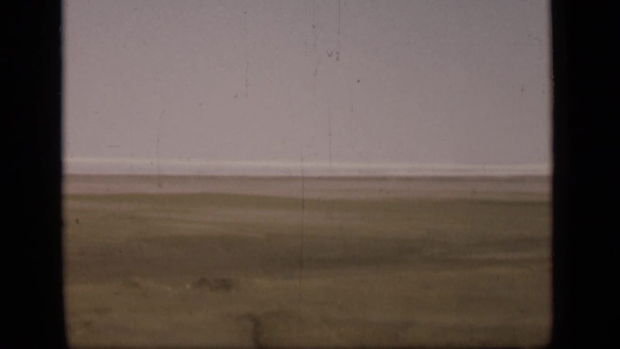 A soft 8mm view of flat terrain near the Suez Canal in Egypt, with muted ground tones and a broad pale sky.