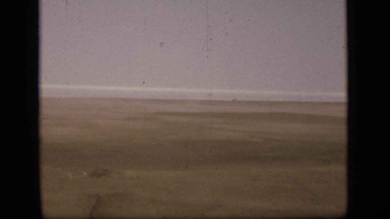 Soft 8mm frame of the Suez Canal region landscape, showing empty desert ground, a distant horizon, and aged film texture.
