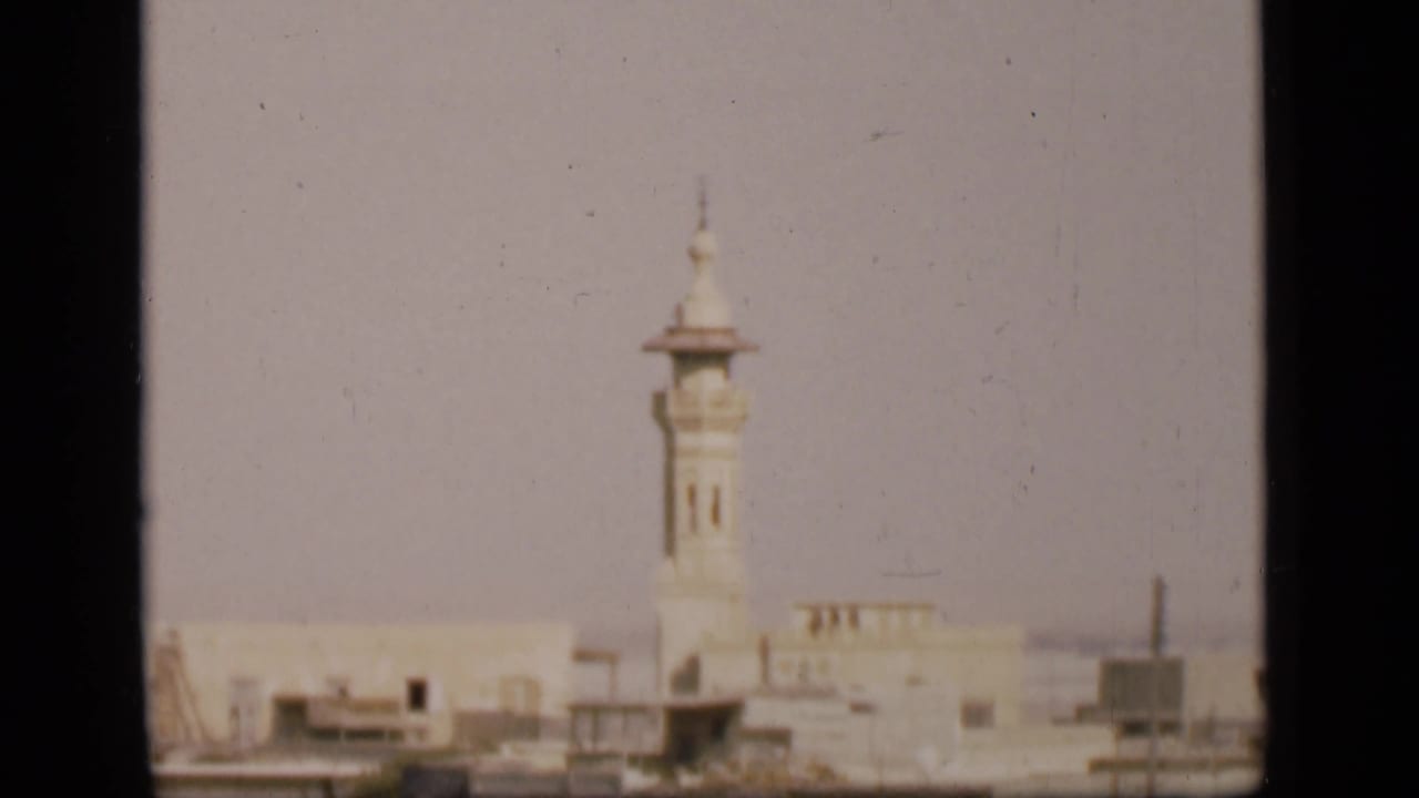 Distant pale minaret above low buildings in a hazy city view.