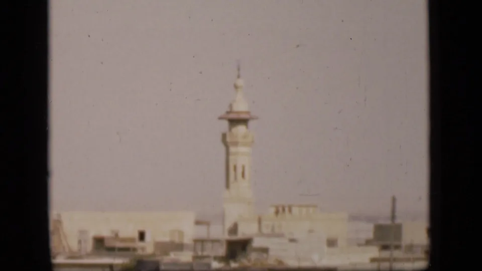 Distant Suez Canal region cityscape on 8mm film, with a pale minaret rising above low flat-roofed buildings.