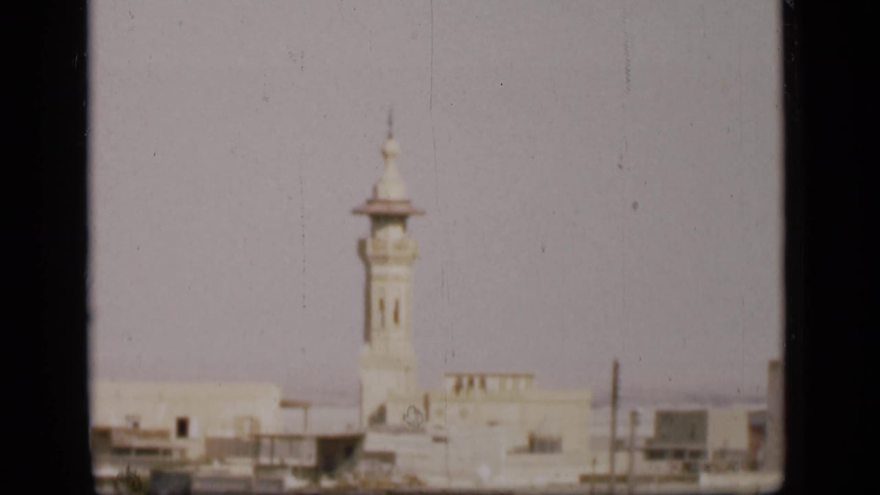 Final 8mm frame of the Suez Canal region cityscape, with a pale minaret, low buildings, and visible film-frame borders.
