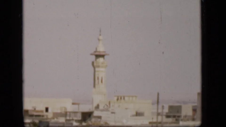 Final 8mm frame of the Suez Canal region cityscape, with a pale minaret, low buildings, and visible film-frame borders.