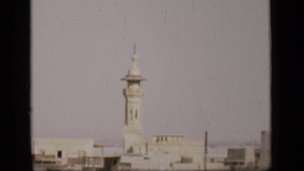 White minaret above low buildings under a pale sky with dark film borders.