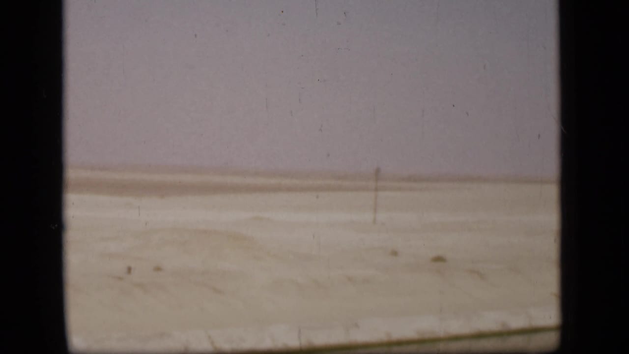 Flat sandy landscape with a distant horizon and a vertical pole.