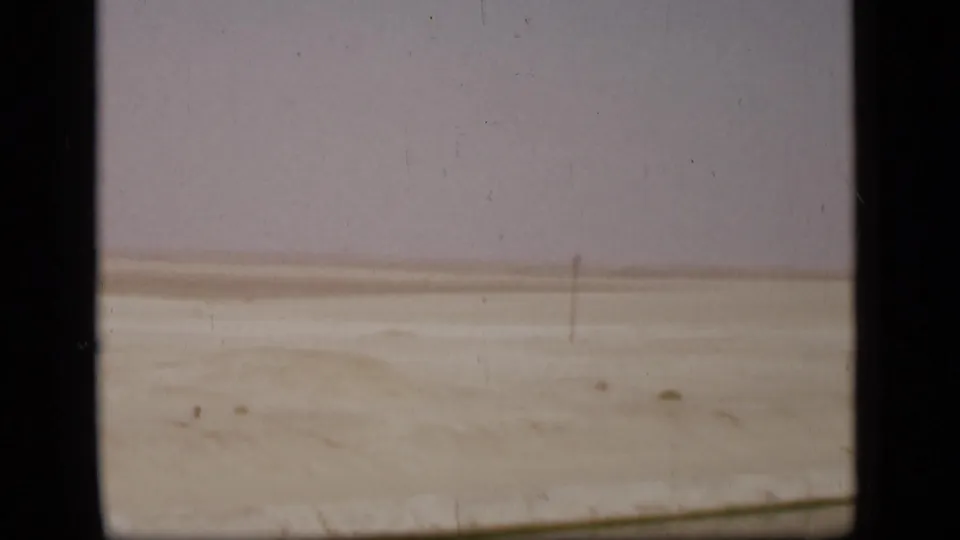 Sandy Suez Canal region landscape with a low horizon, sparse pole, and faded 8mm color during the pan away from the minaret.